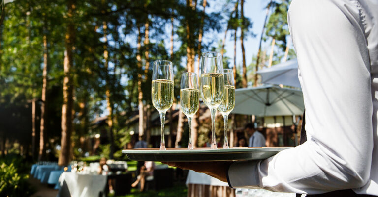 Waiter serving champagne at outdoor wedding event with professional alcohol service