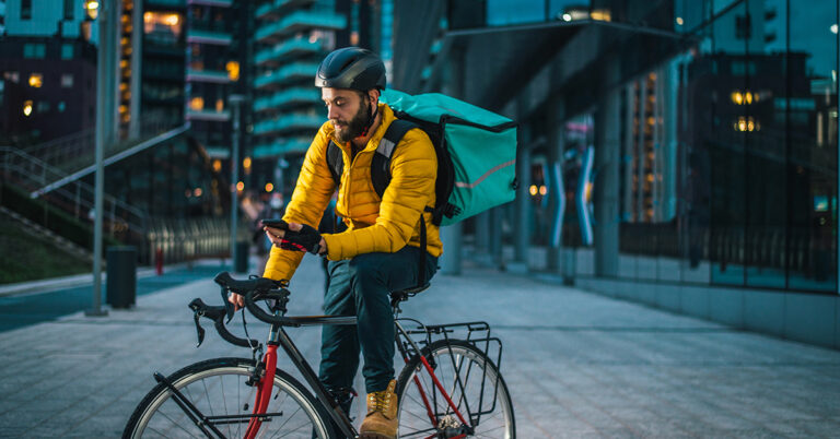 Oregon alcohol delivery driver on bicycle checking phone directions on a Portland street with insulated cold bag