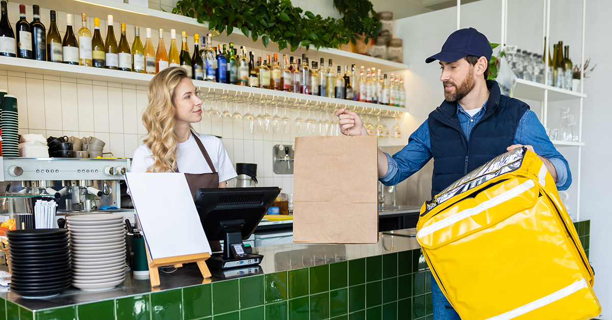Oregon alcohol delivery order being handed from a cafe worker to a courier with an insulated delivery bag