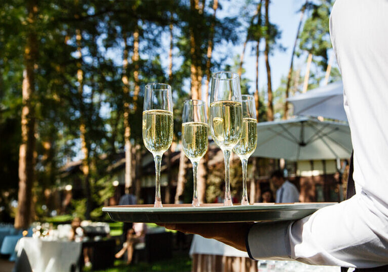 Waiter serving champagne at outdoor wedding event with professional alcohol service